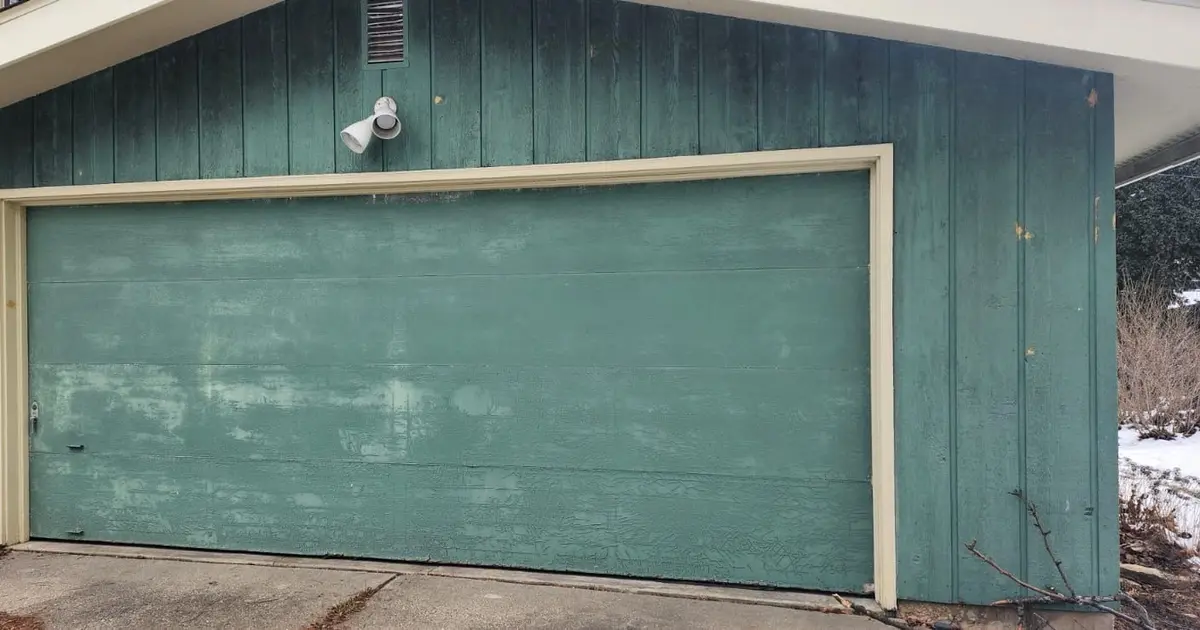 Before: weathered green garage door on a green sided home