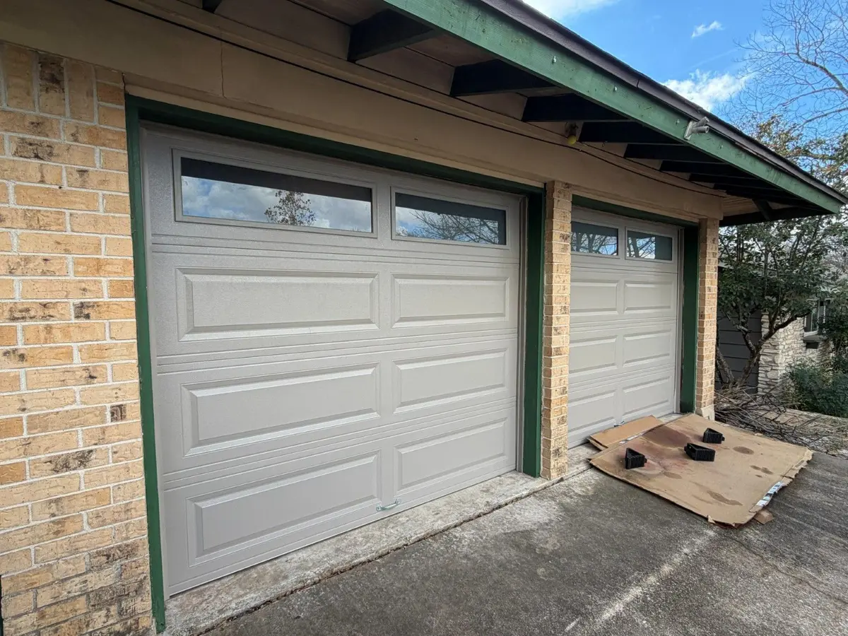Grey long panel garage doors with top windows on a brick home