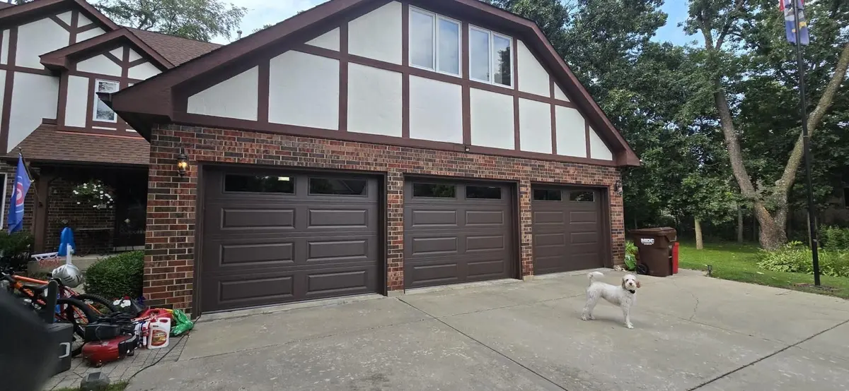 Three dark garage doors with windows on a Tudor style brick home