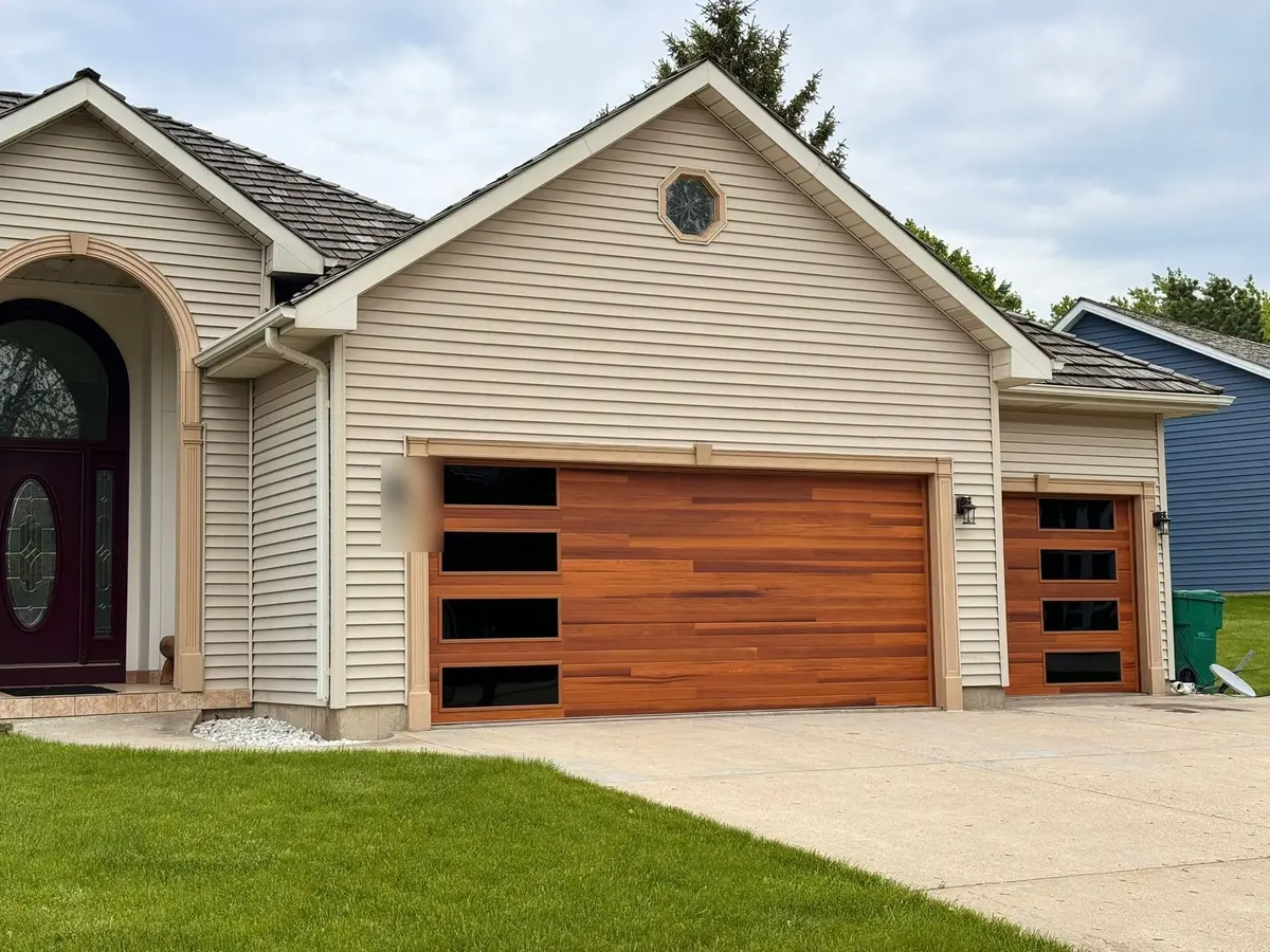 Wood tone modern garage doors with black side windows on a cream sided home