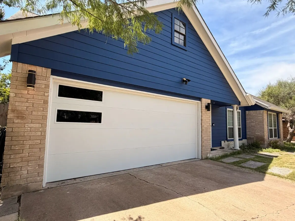 White flush modern garage door with two black side windows installed by Tier One on a blue home with brick columns in Austin 78745