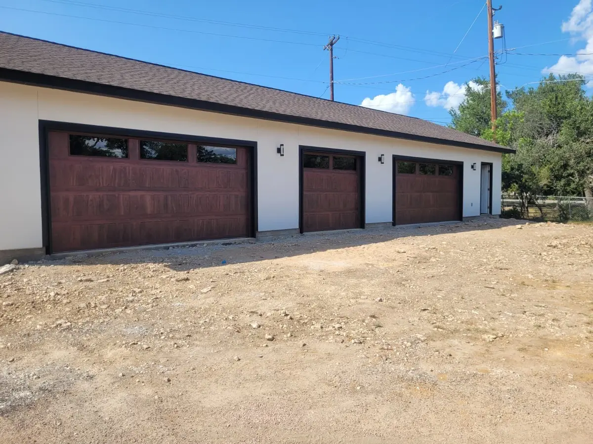 Three wood tone garage doors with windows on a new white detached garage in Hudson Bend, installed by Tier One
