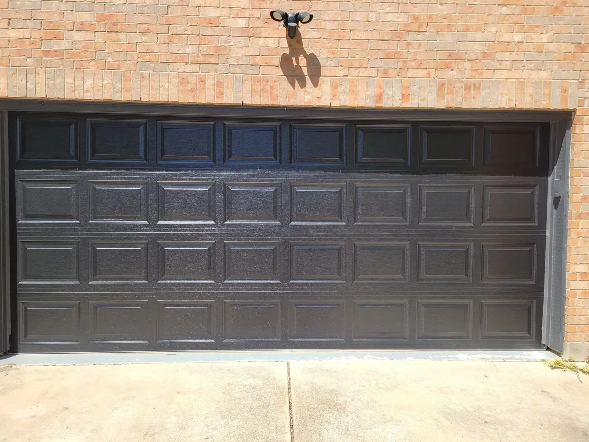 Black raised panel double garage door installed by Tier One on a brick Pflugerville home