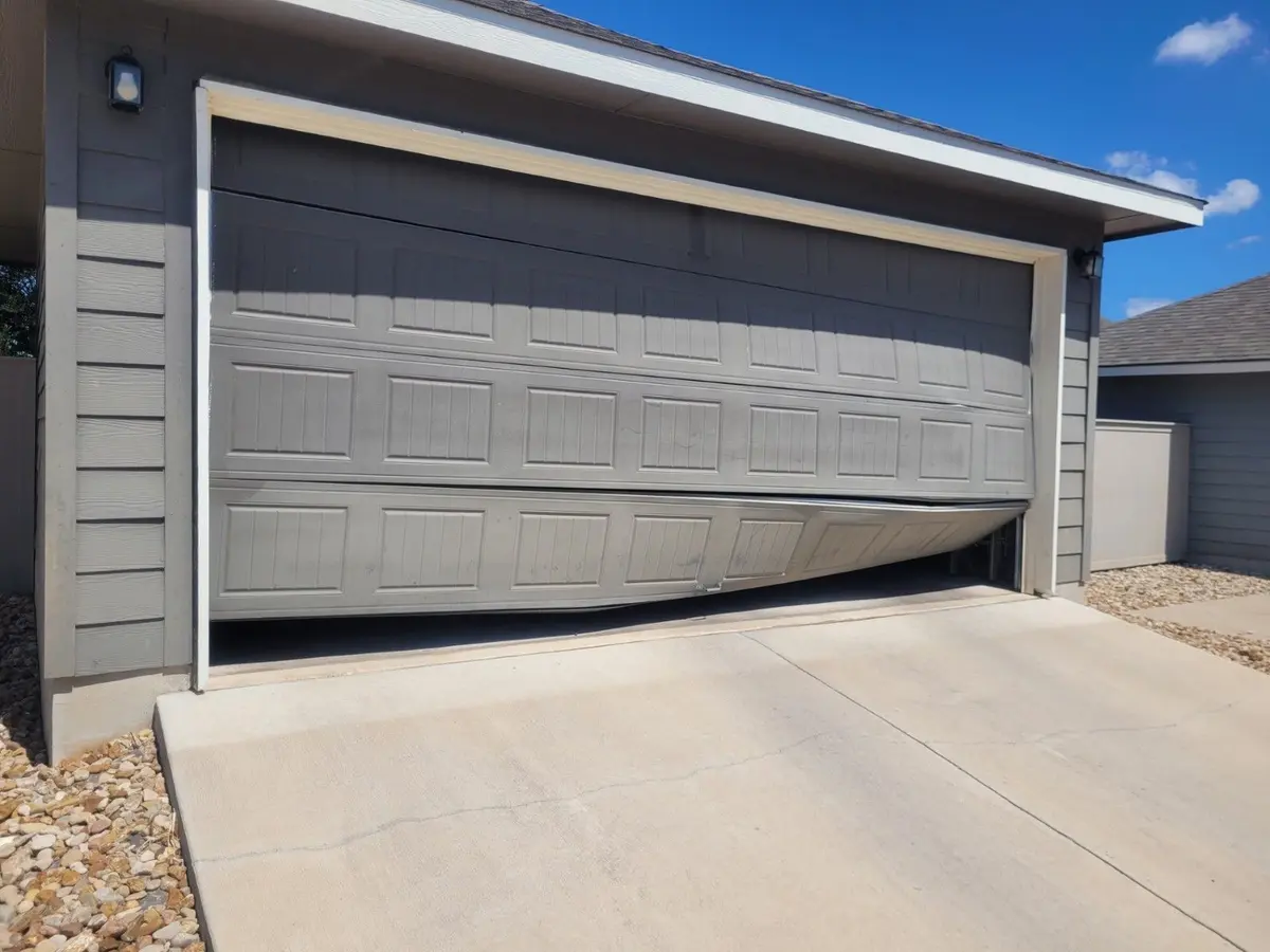 Grey garage door bowed outward and off its track at one side