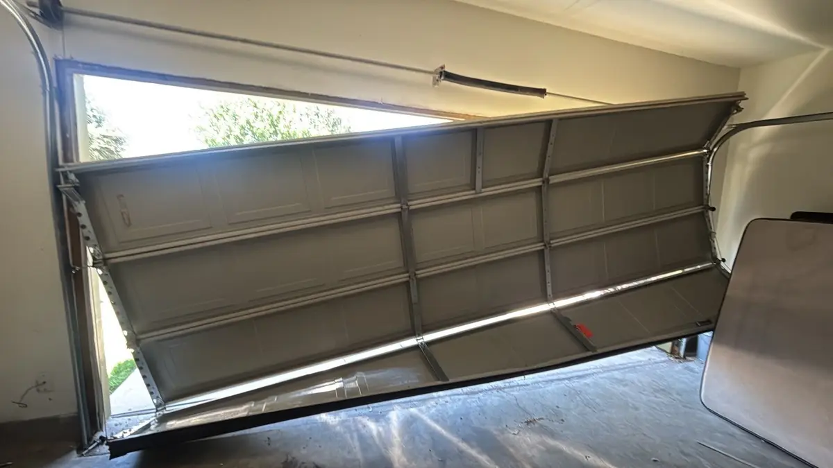 Inside view of a garage door jammed at an angle with its rollers out of the track