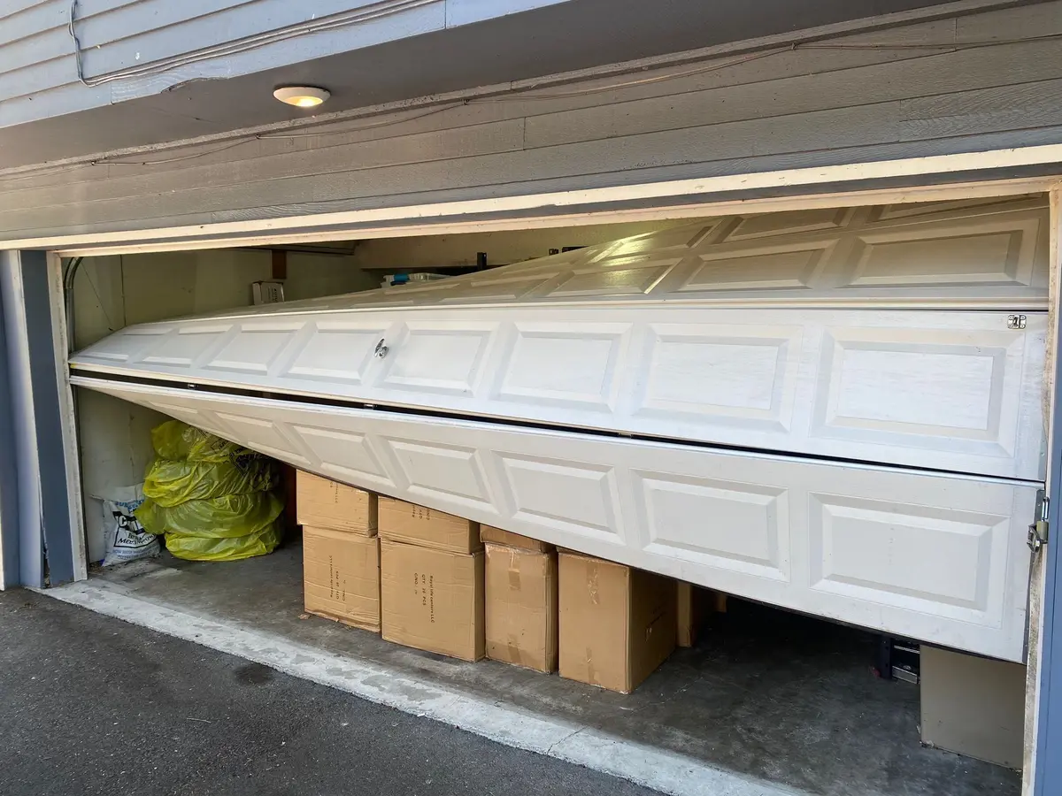 Garage door sections folded and hanging out of the opening before repair