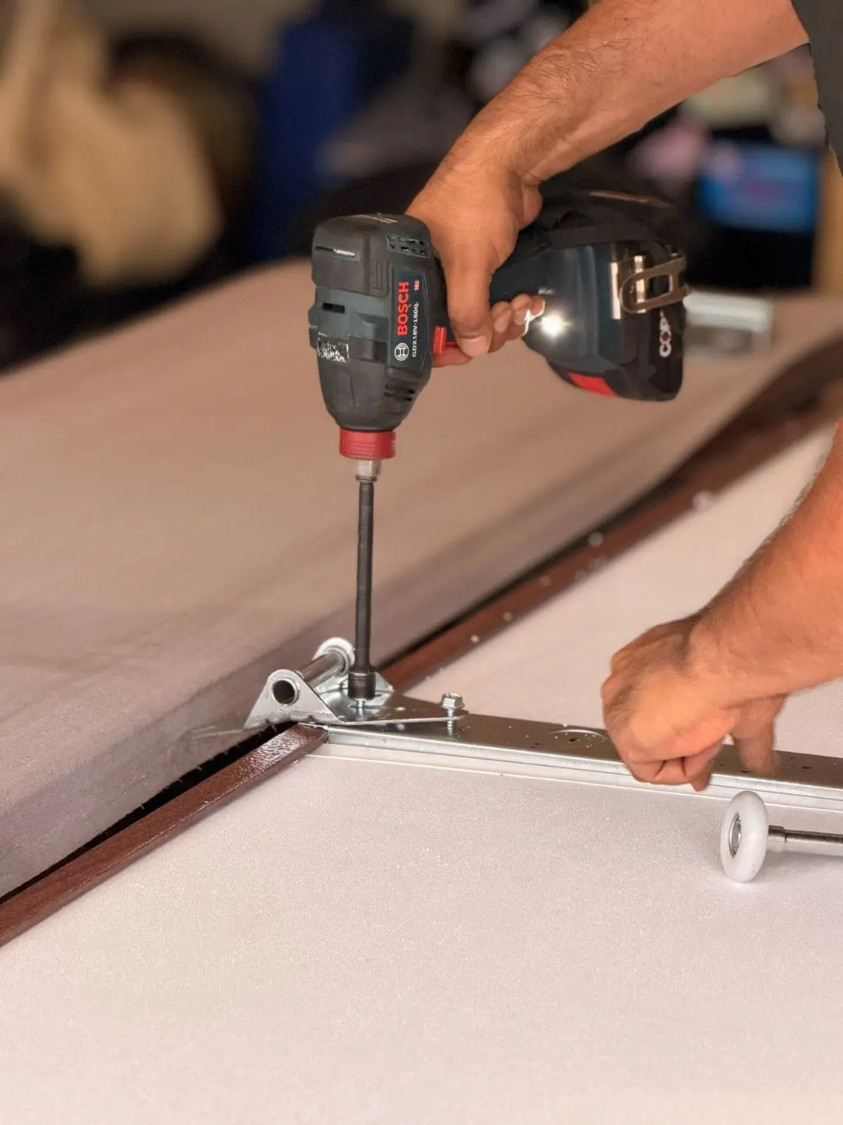 Technician fastening a hinge to a new garage door section with a drill