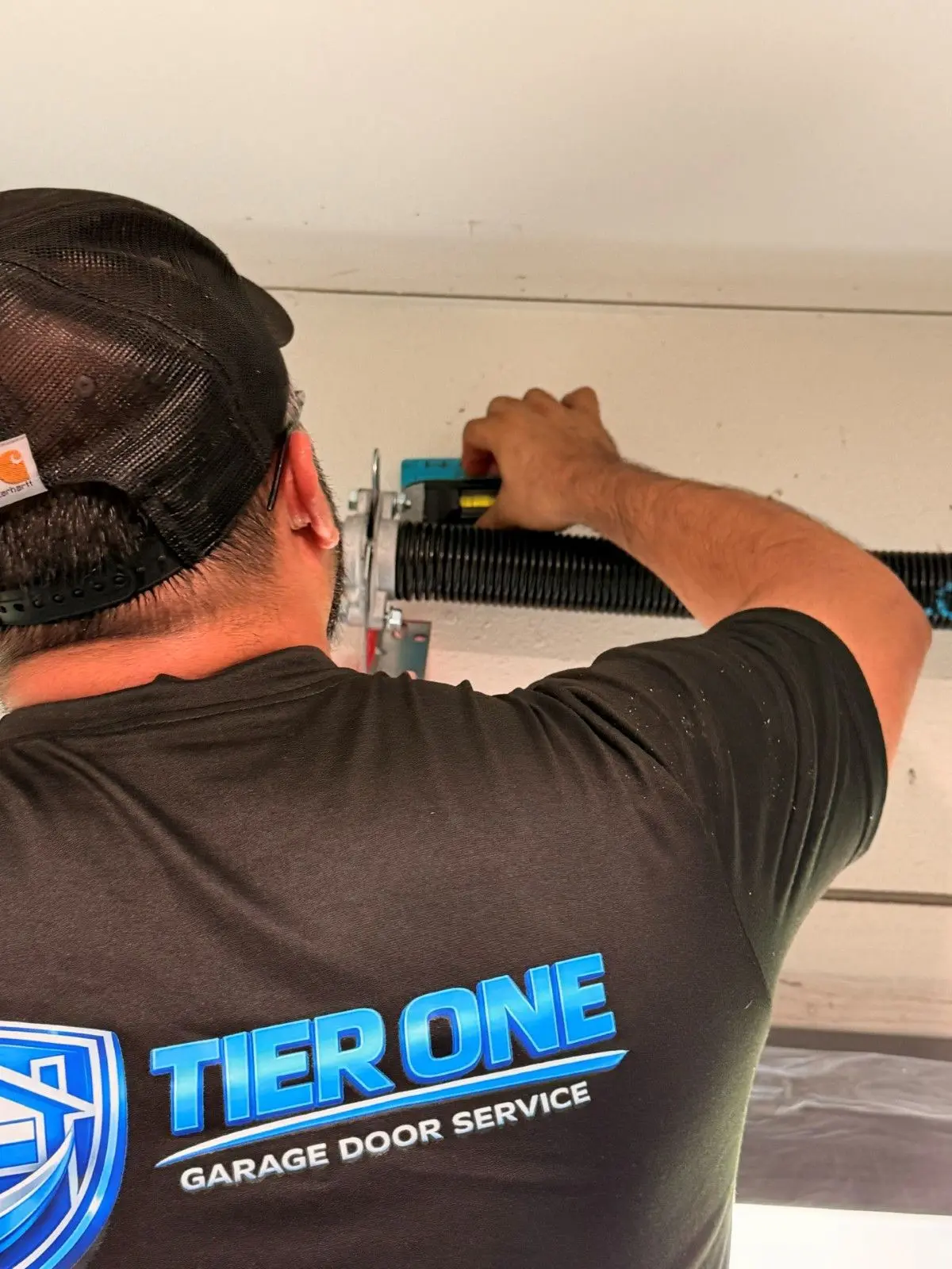 Tier One technician in a company shirt fastening hardware above a garage door