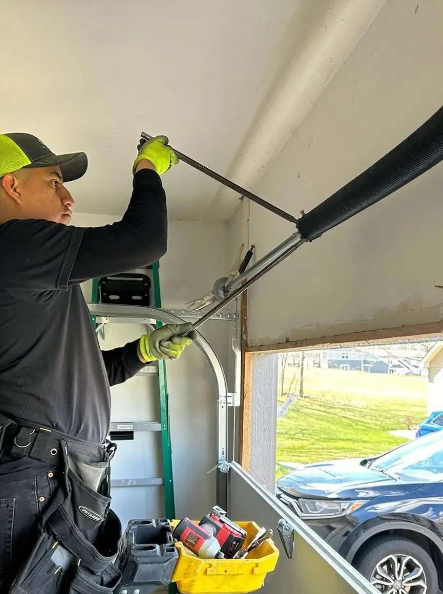 Technician on a ladder using winding bars to tension a new torsion spring above a garage door