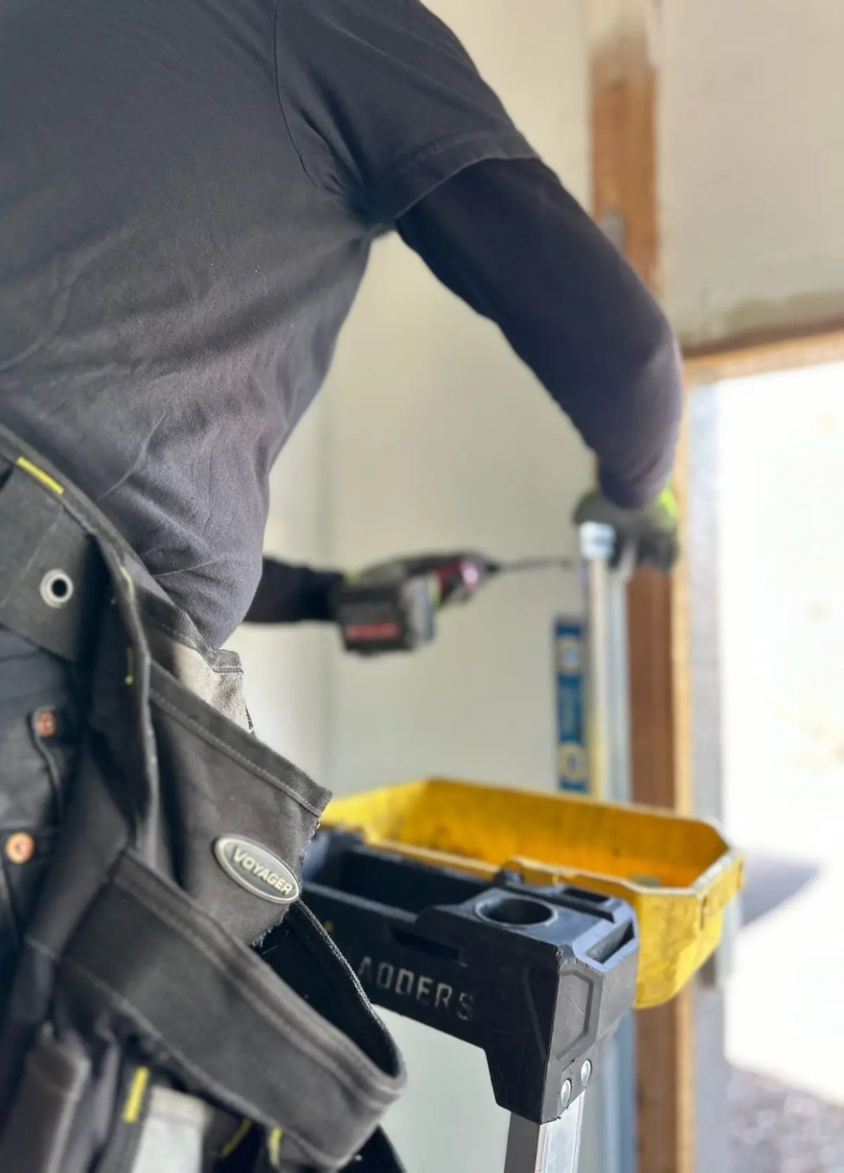Close-up of a technician with a tool belt driving a fastener into a garage door track bracket