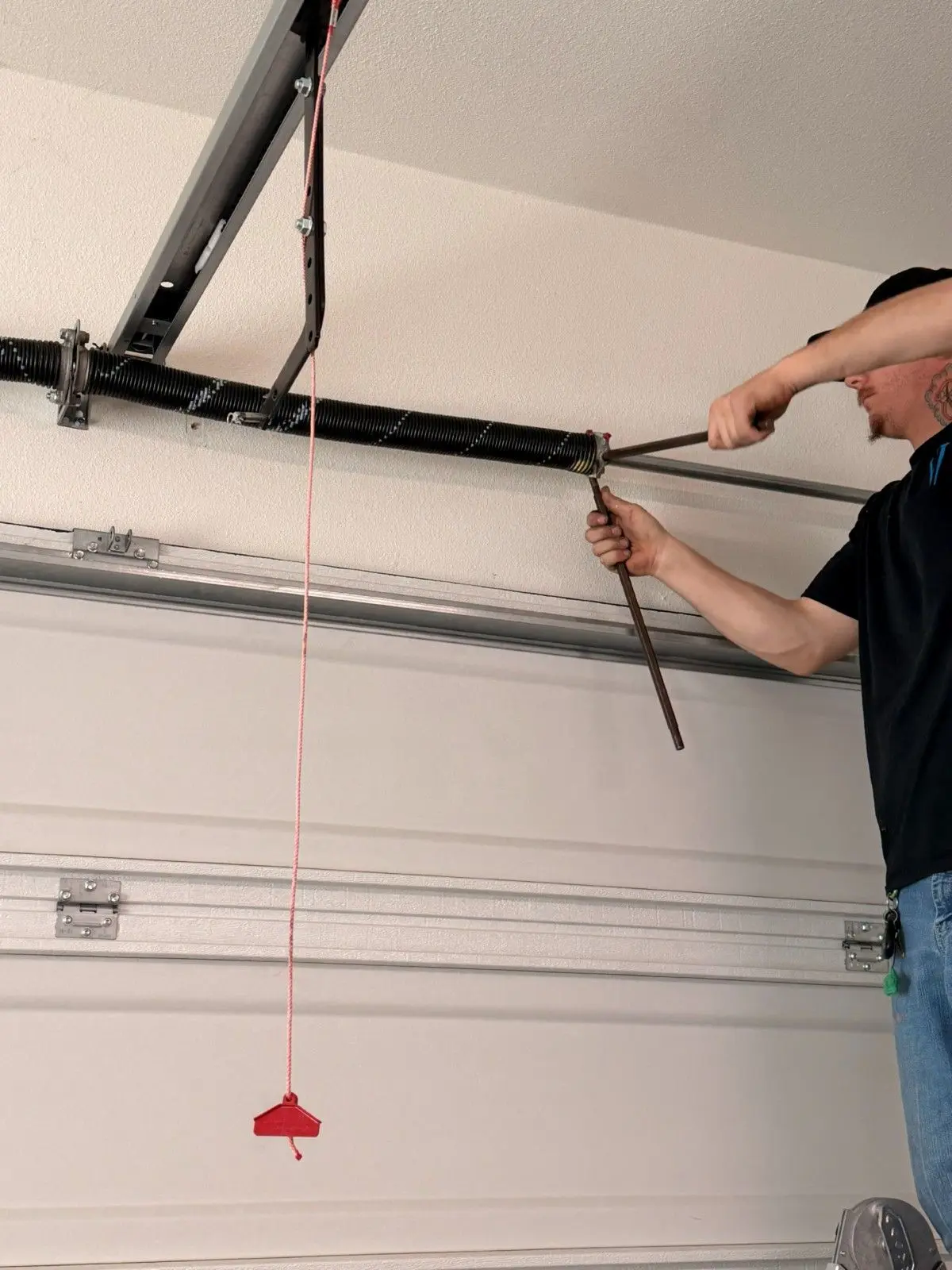 Technician using winding bars to tension a torsion spring above a garage door
