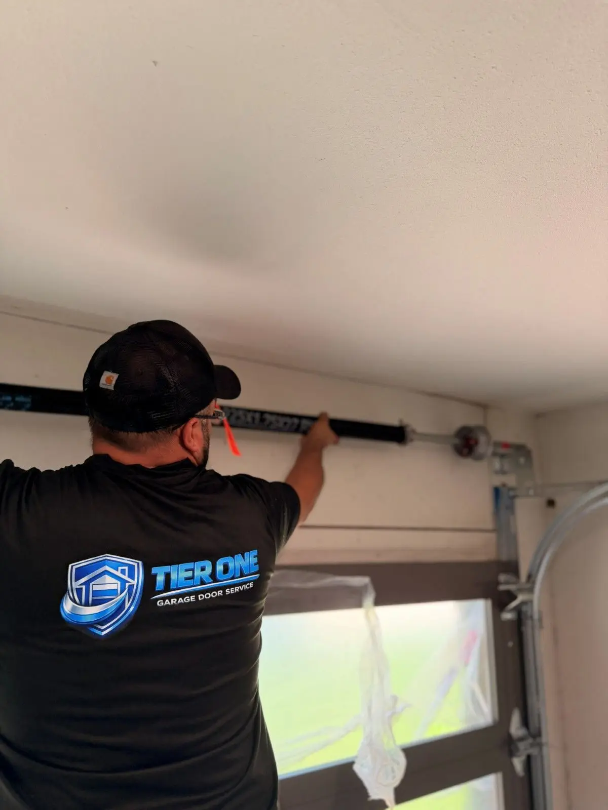 Tier One technician in a company shirt fitting hardware on a full view garage door