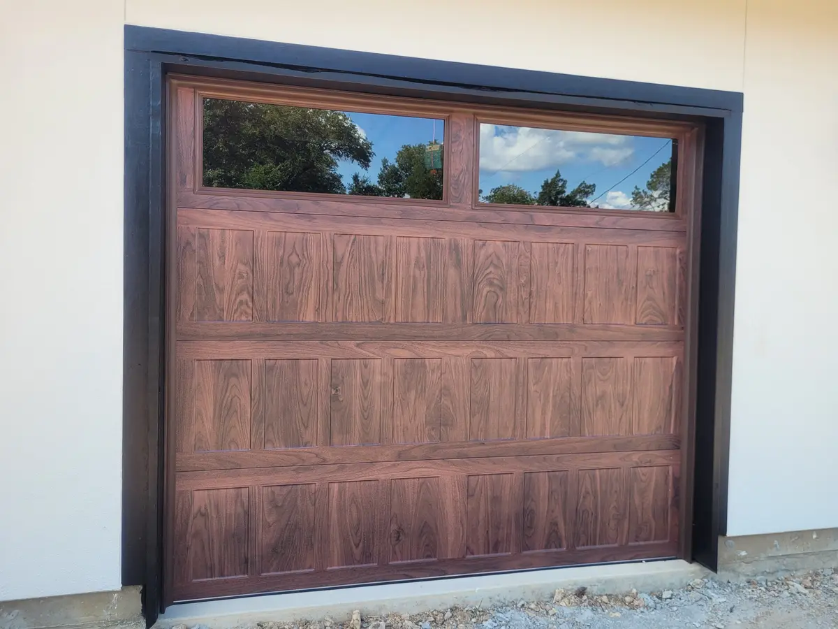 Newly installed wood look steel garage door with a row of windows across the top section
